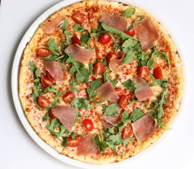 İtalyan mutfağı. Beyaz arka planda jambonlu, roka ve domatesli pizza. Üst görünüm