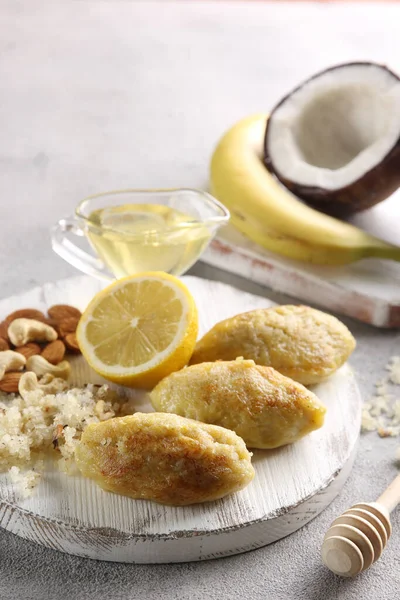 Indian cuisine. Laddoo. Sweet cutlets with coconut shavings, honey, banana, lemon and nuts on a white wooden board. Tropical fruit. Eastern dessert. Background image, copy space