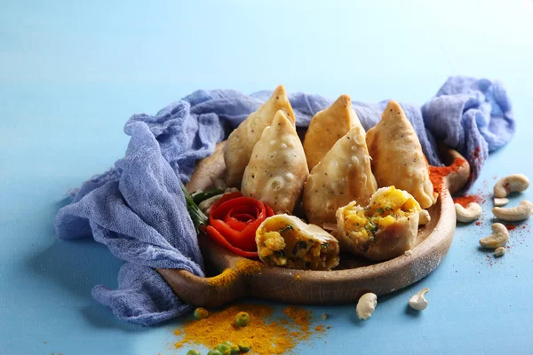 Indian cuisine. Samosa baked pies. Dough with a filling of chicken, potatoes, peas, onions and lentils. Nuts, paprika and turmeric on a blue background. Background image, copy space