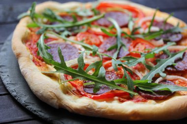 İtalyan mutfağı konsepti, sosisli pizza ve ahşap arka planda roka.
