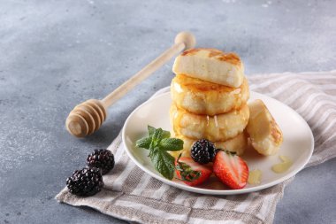 Rus ve Ukrayna mutfağı. Kahvaltıda. Süzme peynirli krep. Ballı cheeseccakes, taze çilek, böğürtlen ve nane şekeri açık gri arka planda beyaz bir tabakta. Boşluğu kopyala