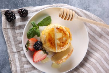 Rus ve Ukrayna mutfağı. Kahvaltıda. Süzme peynirli krep. Ballı cheeseccakes, taze çilek, böğürtlen ve nane şekeri açık gri arka planda beyaz bir tabakta. Boşluğu kopyala