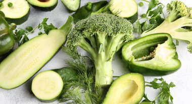 Yeşil sebzeler, hafif arka planda meyveler ve otlar. Taze biber, kabak, bezelye, salatalık, avokado, limon, brokoli, maydanoz, dereotu ve ıspanak. Yiyecek arka planı. Arkaplan resmi