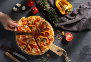 İtalyan mutfağı. Mozarellalı pizza, sarı biber, domates ve kekik gri arka planda tahta bir tahtada. Elleri olan sebzeli pizza. Taşralı. Arkaplan resmi, alanı kopyala