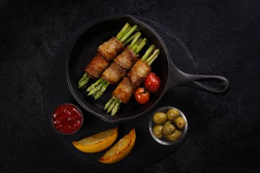 Kızarmış pastırma ve kuşkonmaz, siyah arka planda demir bir tavada. Kızarmış domates ve limon, yeşil zeytin ve ketçap. Arkaplan resmi, alanı kopyala