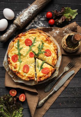 Fransız mutfağı kavramı. Kiş balıklı, domatesli, roka ve peynirli, koyu ahşap zemin üzerinde, zeytinyağı ve yumurtanın yanında. Arkaplan resmi, alanı kopyala