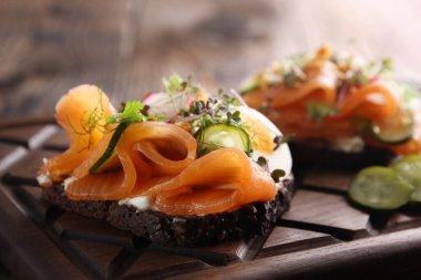 Atıştırmalıklar Kırmızı balıklı sandviç, yumurta, krem peynir, ahşap bir tahtanın üzerinde salatalık ve otlar. Arkaplan resmi, alanı kopyala