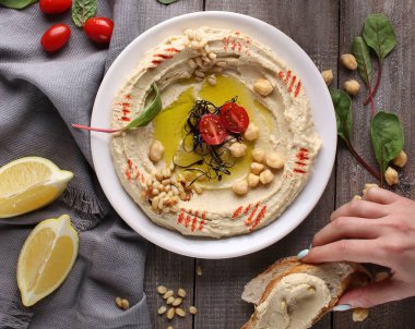 Doğu mutfağı. Geleneksel atıştırmalık humus. İçinde nohut, çam fıstığı, zeytinyağı, baharat ve limon suyu var. Hafif ahşap arka planda bitkiler ve domatesler. Elle sandviç..