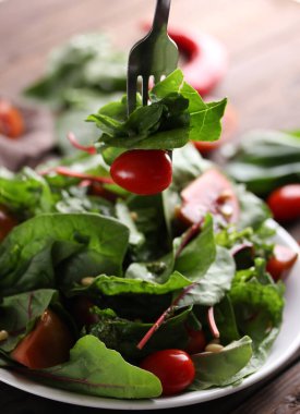 Sağlıklı yiyecekler. Yaprak salatası, ıspanak, pazı, vişneli domates ve ahşap arka planda sos soslu fındık. Beyaz tabak ve çatal.