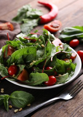 Sağlıklı yiyecekler. Yaprak salatası, ıspanak, pazı, vişneli domates ve ahşap arka planda sos soslu fındık. Beyaz tabak ve çatal.