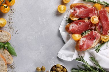 İtalyan mutfağı kavramı. Coppa, domuz boynundan yapılmış İtalyan kurutulmuş sosisi. Atıştırmalık et. Ekmek, zeytin, kiraz domatesleri, biberiye, açık beyaz arka planda fesleğen. Arkaplan resmi, alanı kopyala