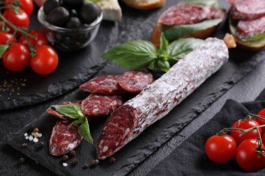 İtalyan mutfağı kavramı. Domates, zeytin, fesleğen ve peynirli siyah tahtada sosis. Sosisli ekmek, sandviç. Arkaplan resmi, alanı kopyala