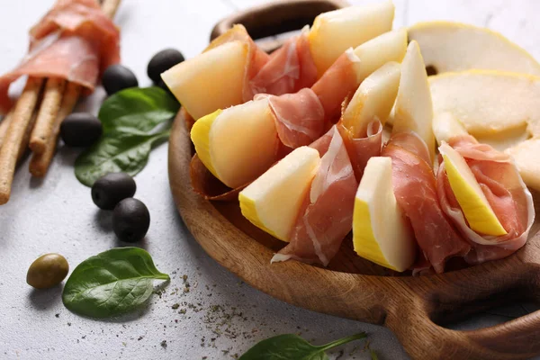 The concept of Italian cuisine. Italian ham. Prosciutto with melon, olives and Parmesan cheese. Spinach and spices on a light grey background. Background image, copy space