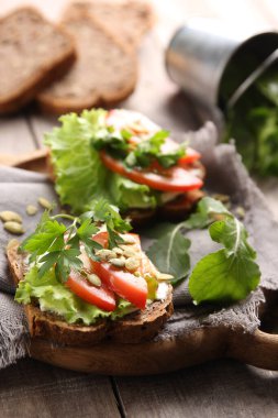Sağlıklı yiyecekler. Krem peynirli ekmek, otlar, marul, domates ve balkabağı tohumlu gri ahşap arka plan. Taşralı. Arkaplan resmi, alanı kopyala