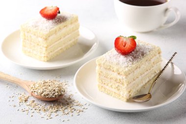 Tatlı. Kremalı beyaz bisküvi keki ve kaşıkla beyaz tabakta hindistan cevizi ezmesi. Hafif arka planda bir fincan kahve ve çilek. Arkaplan resmi, alanı kopyala