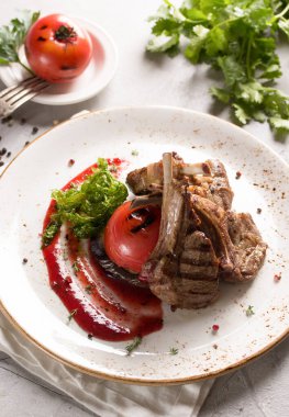 Izgara pirzola, domates ve sosla birlikte beyaz bir tabakta hafif bir arka planda. Bir demet taze kişniş, arka planda ızgara domates. Menü restoranı. Arkaplan resmi, alanı kopyala