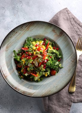 Brokolili yağsız sebze salatası, kırmızı biber, mısır, salatalık ve nar tohumları açık gri arka planda çatalla birlikte kalın bir tabakta. Arkaplan resmi, alanı kopyala