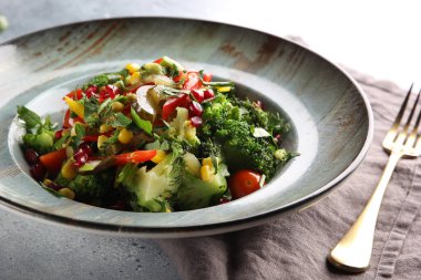 Brokolili yağsız sebze salatası, kırmızı biber, mısır, salatalık ve nar tohumları açık gri arka planda çatalla birlikte kalın bir tabakta. Arkaplan resmi, alanı kopyala