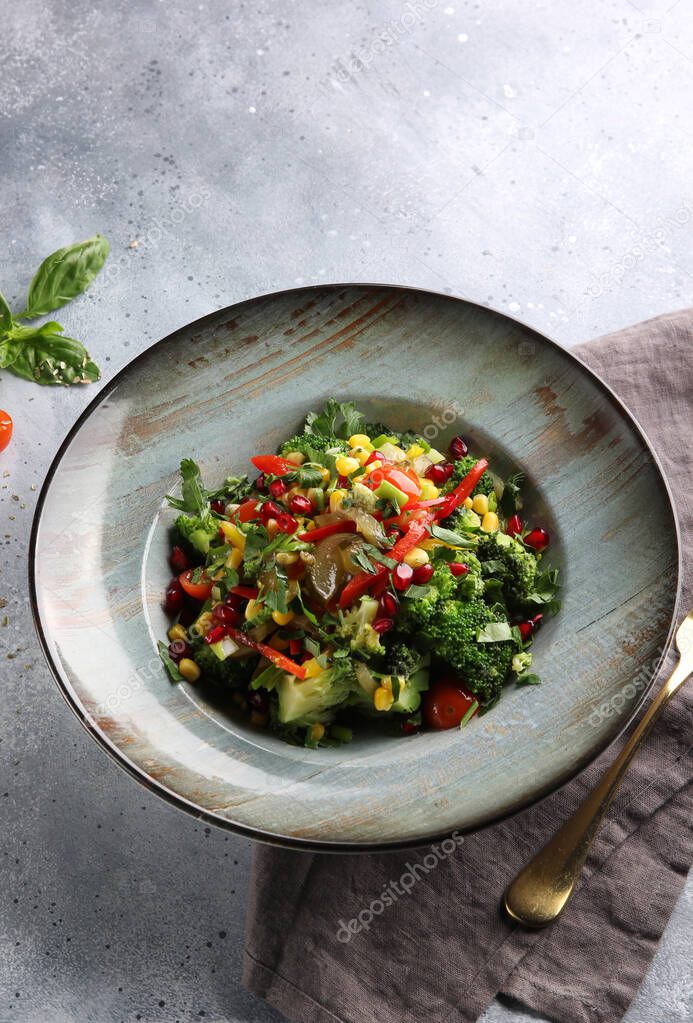 Lean vegetable salad with broccoli, red pepper, corn, cucumber and pomegranate seeds in a deep dish on a light grey background. Background image, copy space