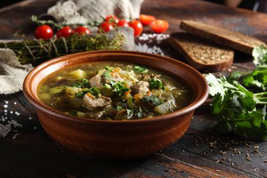 Sebzeli köy çorbası, et ve eski ahşap arka planda kil kasede taze otlar. Ekmek, kimyon, kişniş, domates, kaşık ve biraz da dereotu. Arkaplan resmi, alanı kopyala 