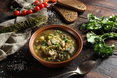 Sebzeli köy çorbası, et ve eski ahşap arka planda kil kasede taze otlar. Ekmek, kimyon, kişniş, domates, kaşık ve biraz da dereotu. Arkaplan resmi, alanı kopyala 