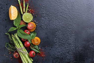 Taze çiğ sebzeler ve otlar, kuşkonmaz, kırmızı kiraz domatesleri, sarı domatesler, limon, ıspanak, fesleğen ve baharatlar siyah arka planda. Üst Manzara, düz çizgi. Arkaplan resmi, alanı kopyala 