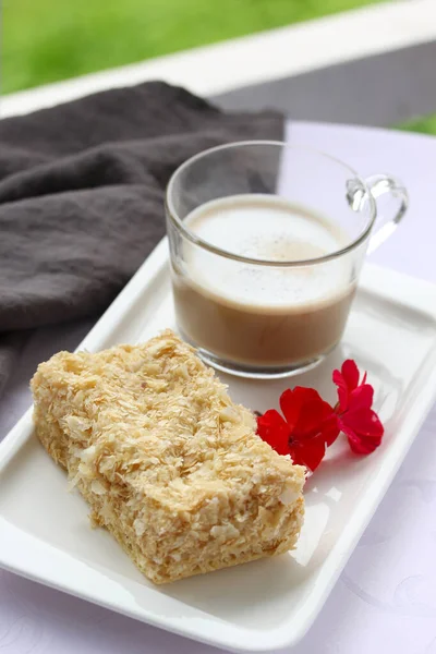 Desserts, a cup of coffee and napoleon cake on a white plate on the table. Purple flower. Background image, copy space