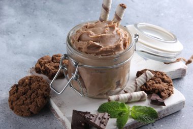 Tatlı. Tiramisu, şeffaf bir kavanozda, beyaz tahta üzerinde kurabiye, nane ve çikolata bulunan kahverengi macun. Arkaplan resmi, alanı kopyala 