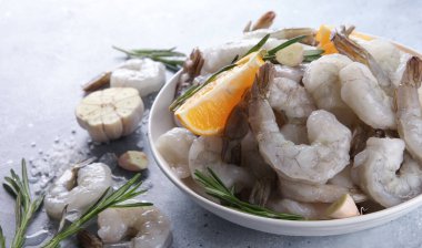 Deniz ürünleri. Çiğ yeşil kraliyet karidesleri beyaz tabakta karides, biberiye, limon, sarımsak ve tuz açık gri arka planda. Arkaplan resmi, alanı kopyala 