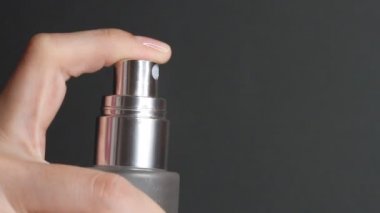 Parfüm sıkma ya da termal su şişesi. Siyah arka planda kozmetik şişesi pompasını iten parmak..