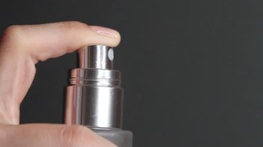 Parfüm sıkma ya da termal su şişesi. Siyah arka planda kozmetik şişesi pompasını iten parmak..