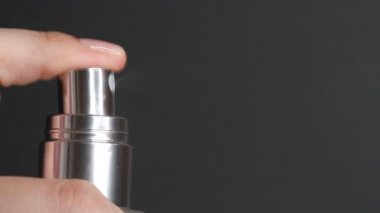 Parfüm sıkma ya da termal su şişesi. Siyah arka planda kozmetik şişesi pompasını iten parmak..
