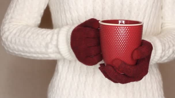 Young woman in white sweater is holding red cup of tea or coffee. Changing hand, trying to warm hands with hot drink — Stock Footage Young Woman White Sweater Holding Red Cup Tea Coffee Changing Stock Video