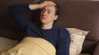 Sick young caucasian hipster man is lying in the bed cough and sneeze. Cold and flu, high body temperature