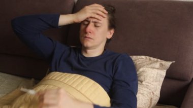 Sick young caucasian hipster man is lying in the bed cough and sneeze. Cold and flu, high body temperature