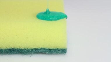Blue dish washing liquid gel is pouring on yellow sponge on white background 