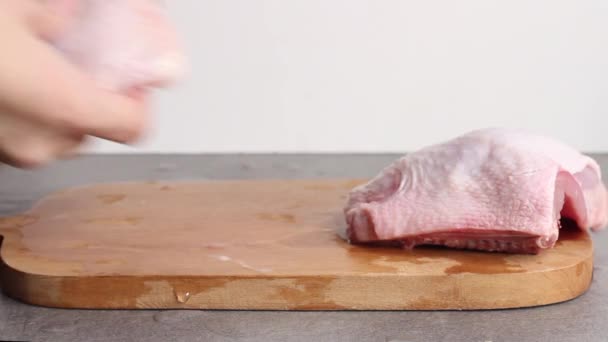 Vrouw zet rauwe kip dij met kruiden op snijplank op grijze tafel. — Stockvideo