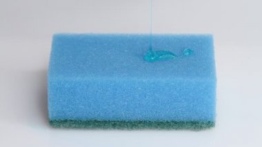 Blue dish washing liquid gel is pouring on blue sponge on white background 