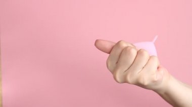 Pembe arka planda tekrar kullanılabilir pembe silikon adet bardağını tutan genç bir kadının ellerini yakın plan. Sıfır atık adet hijyen konsepti.