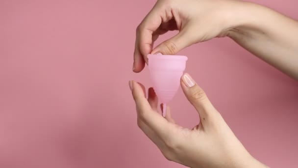 ピンクの背景に再利用可能なピンクのシリコーン生理カップを保持している若い女性の手のクローズアップ 廃棄物ゼロ月経衛生コンセプト — ストック動画