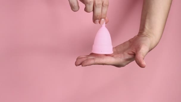 Detailní záběr mladé ženy ruce drží opakovaně použitelný růžový silikonový menstruační pohár na růžovém pozadí. Koncepce hygieny nulového odpadu.