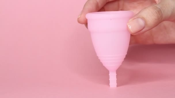 Detailní záběr mladé ženy ruce drží opakovaně použitelný růžový silikonový menstruační pohár na růžovém pozadí. Koncepce hygieny nulového odpadu.