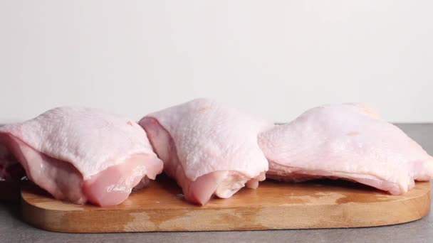 Woman puts Raw chicken thigh with herbs on cutting board on grey table. — Stock Video