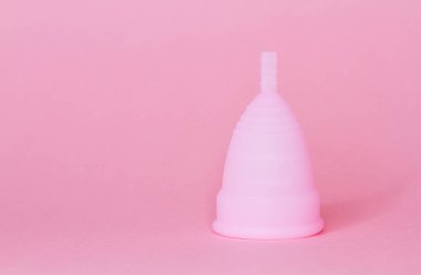 Yeniden kullanılabilir pembe silikon regl bardağını pembe arka planda tutan kadın elleri