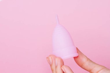 Yeniden kullanılabilir pembe silikon regl bardağını pembe arka planda tutan kadın elleri