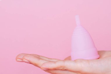 Yeniden kullanılabilir pembe silikon regl bardağını pembe arka planda tutan kadın elleri