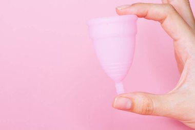 Yeniden kullanılabilir pembe silikon regl bardağını pembe arka planda tutan kadın elleri