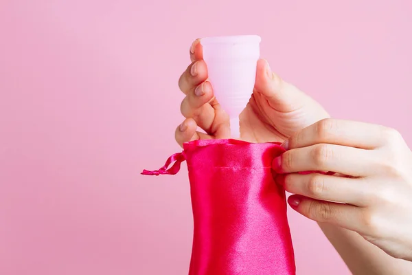 Mulheres mãos segurando copo menstrual de silicone rosa reutilizável no fundo rosa — Fotografia de Stock