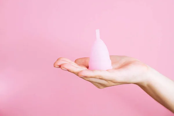 Mulheres mãos segurando copo menstrual de silicone rosa reutilizável no fundo rosa — Fotografia de Stock