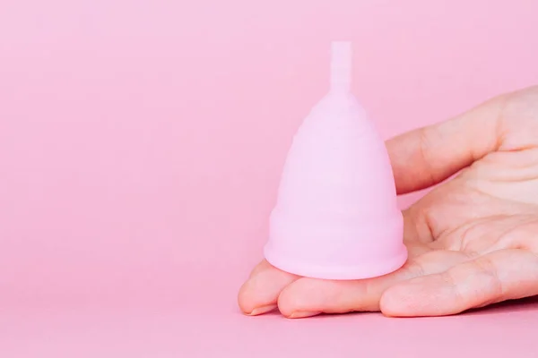 Mulheres mãos segurando copo menstrual de silicone rosa reutilizável no fundo rosa — Fotografia de Stock